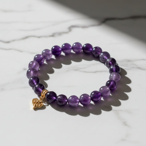 Purple beaded bracelet with a gold heart charm on a wooden surface
