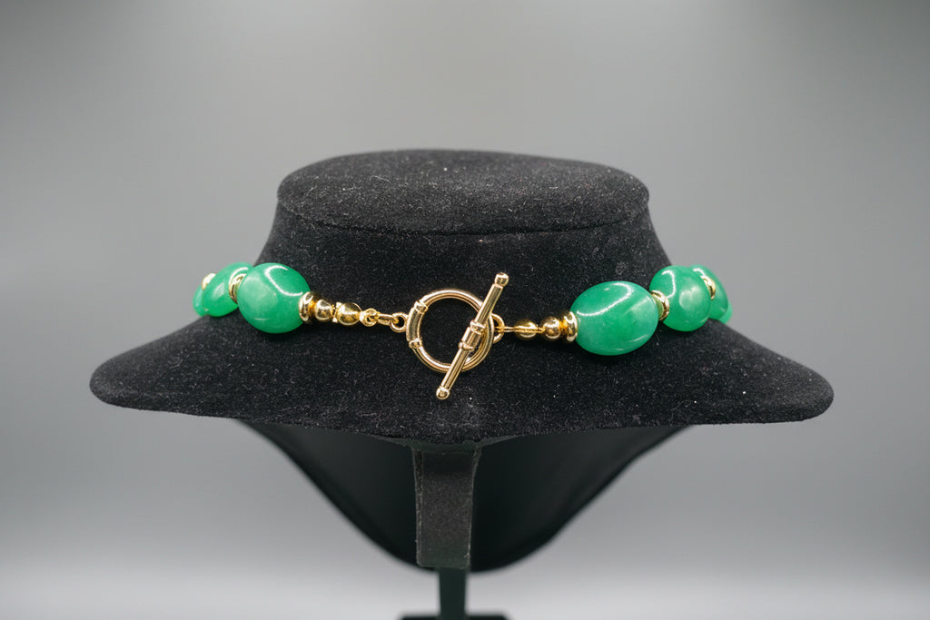Green beaded bracelet with gold clasp on a black stand against a green background