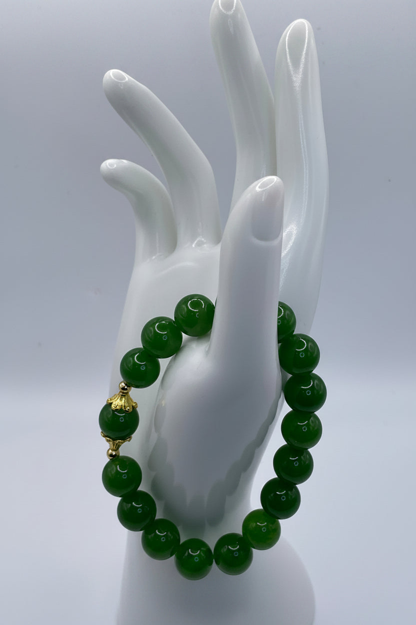 A green beaded bracelet with a gold accent bead, displayed on a white ceramic hand mannequin against a light gray background.