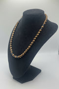A beaded necklace featuring faceted red bronze hematite beads with black hematite spacers, displayed on a black velvet jewelry bust.