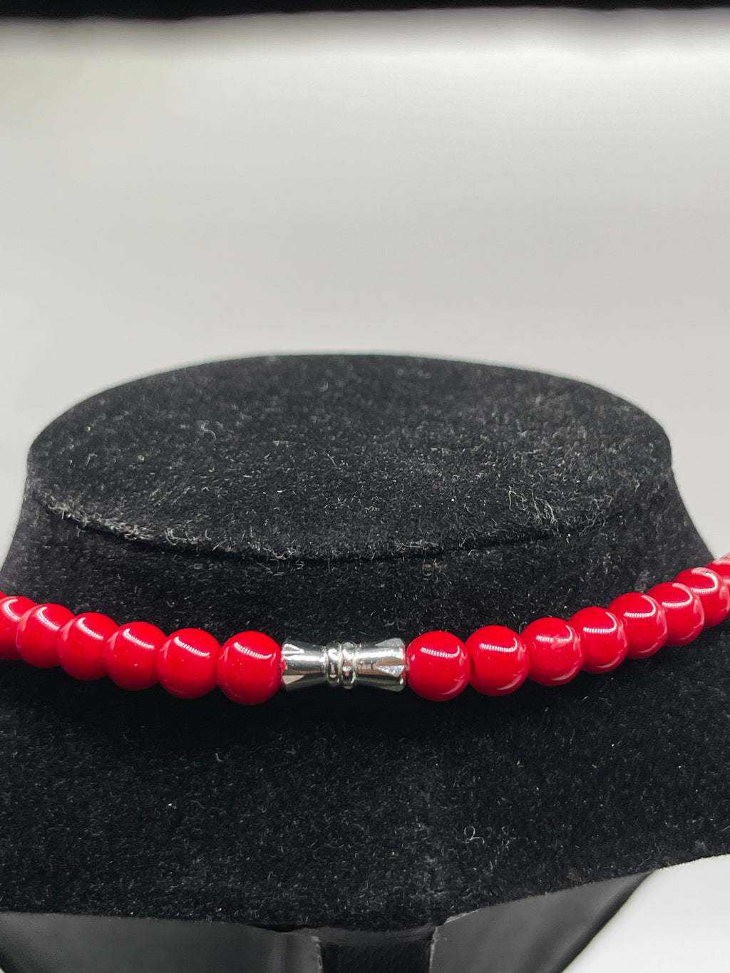 Red beaded bracelet with a silver clasp on a black stand against a white background