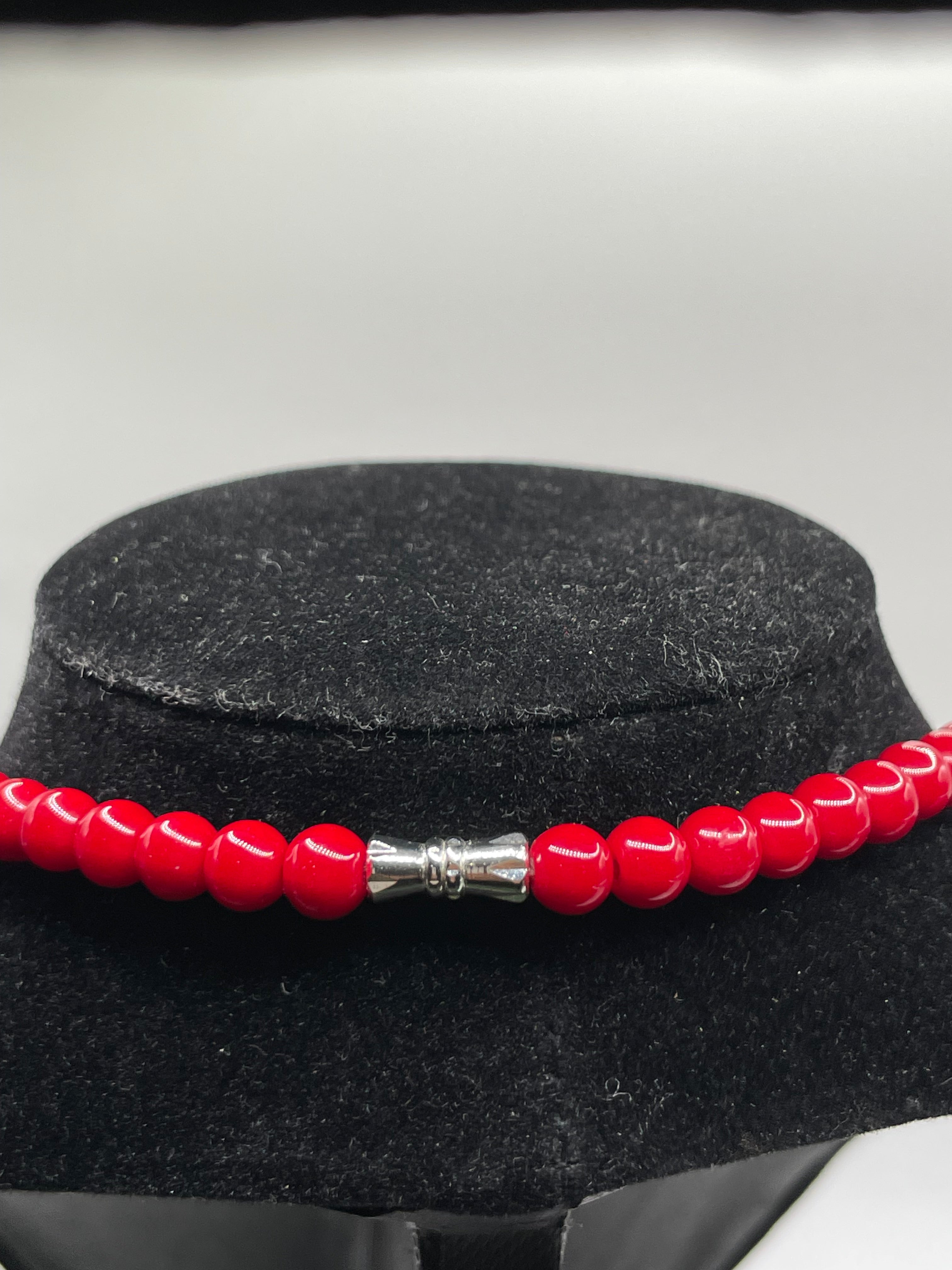 Red beaded bracelet with a silver clasp on a black stand against a white background