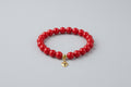 Red beaded bracelet with a gold heart charm on a wooden surface