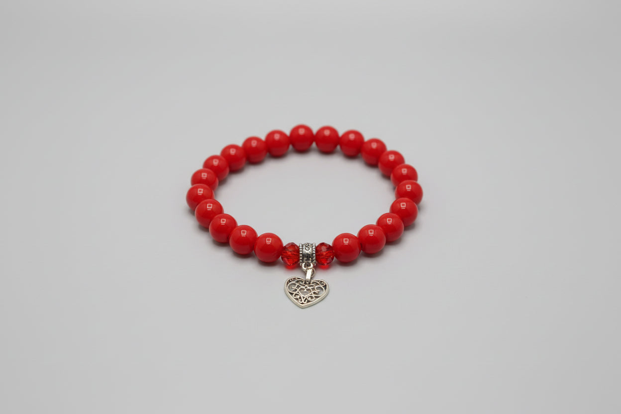 Red beaded bracelet with a silver  heart charm on a wooden surface