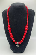 Red beaded necklace with a silver heart charm on a black mannequin bust.