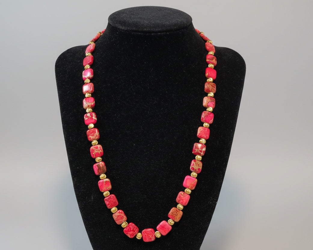 Necklace with red and gold beads on a black stand