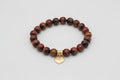 Bracelet with red tiger beads and a heart-shaped charm on a wooden surface