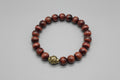Bracelet with red beads and a gold charm on a wooden surface