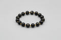 Black beaded bracelet with gold small round spacers on a light gray background