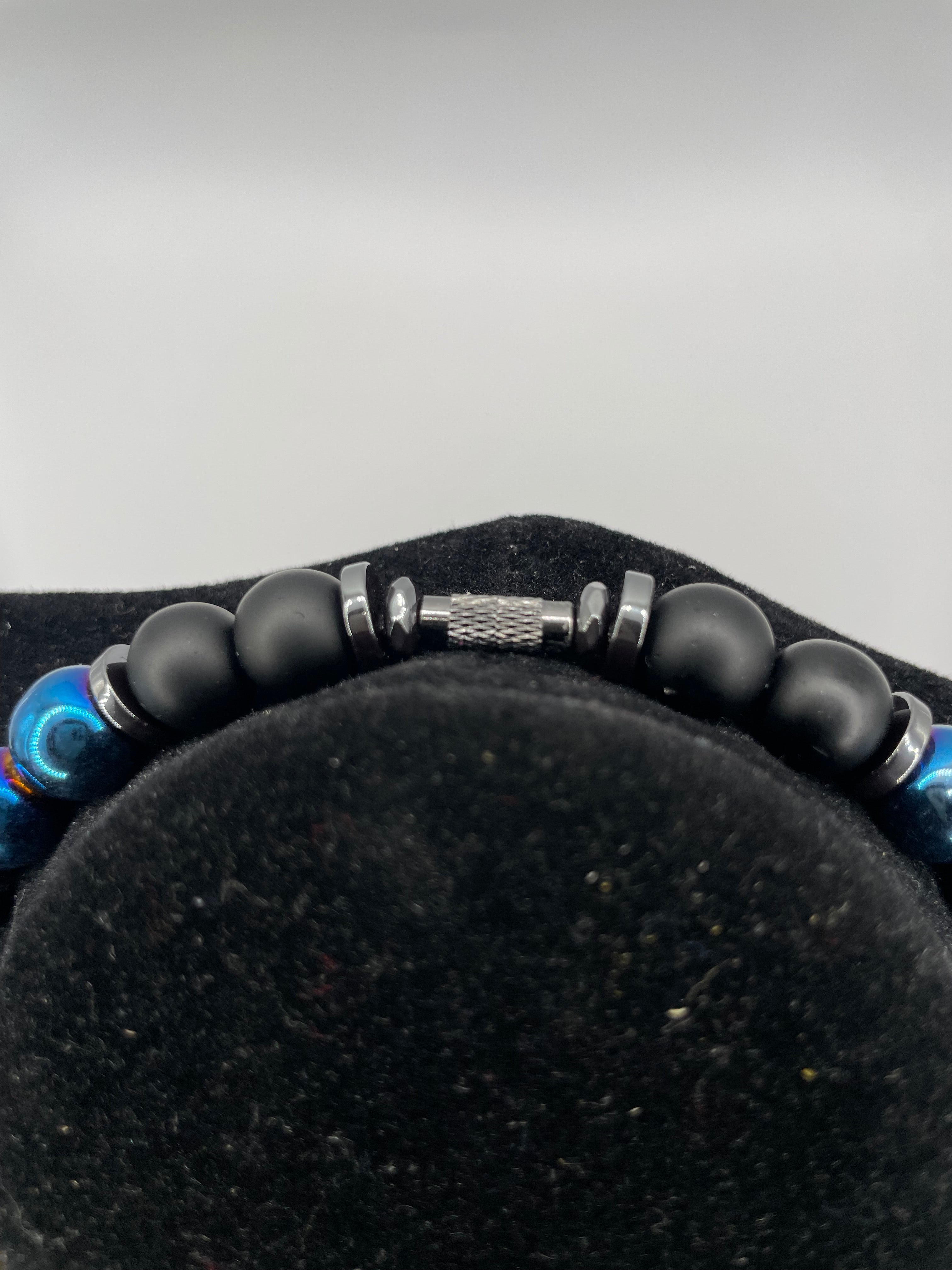 Close-up of a beaded bracelet with black beads and metal accents on a black cushion.