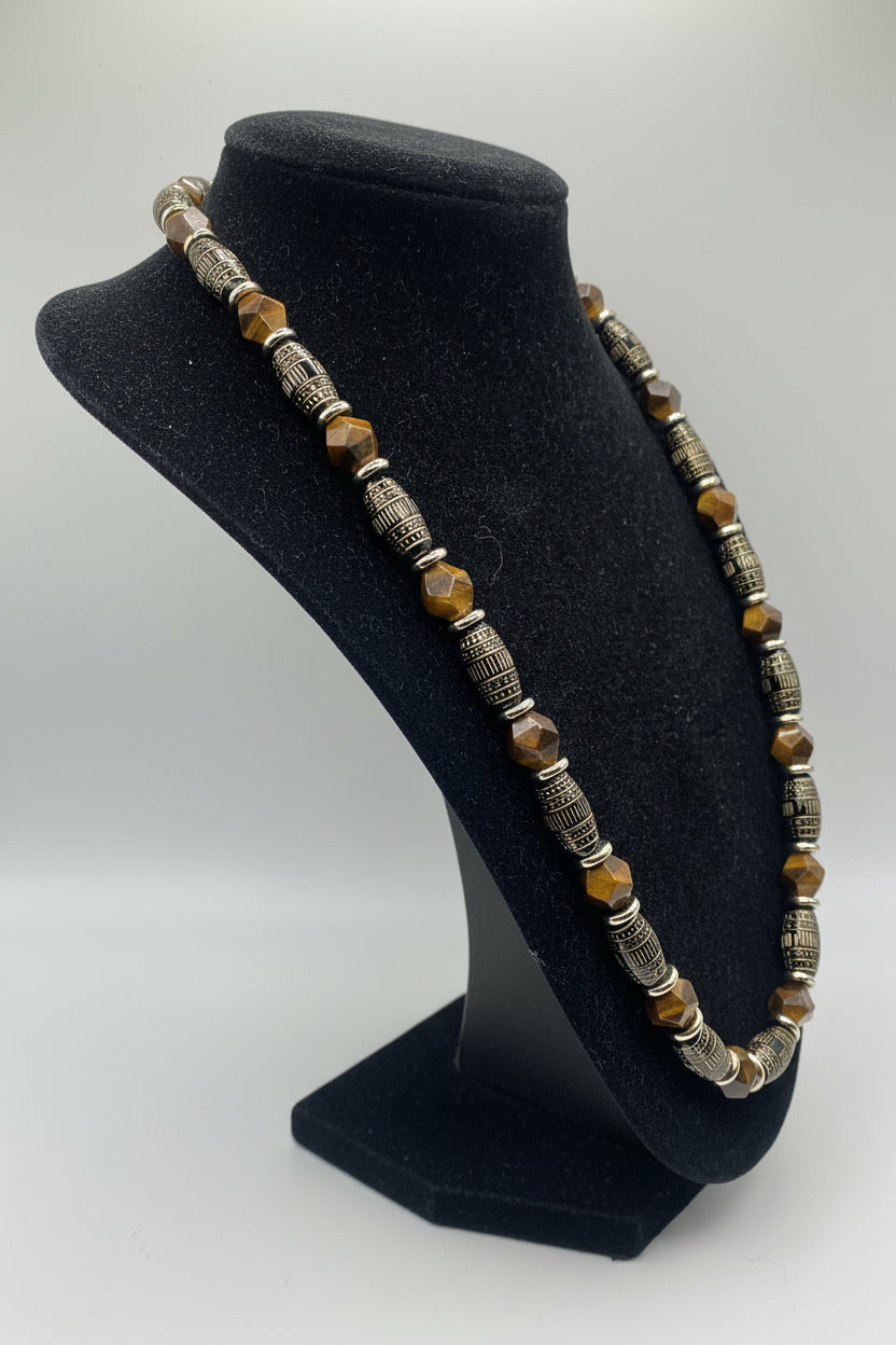 A beaded necklace displayed on a black velvet jewelry bust. The necklace features alternating metallic silver filigree spacers and faceted brown and amber-orange beads.