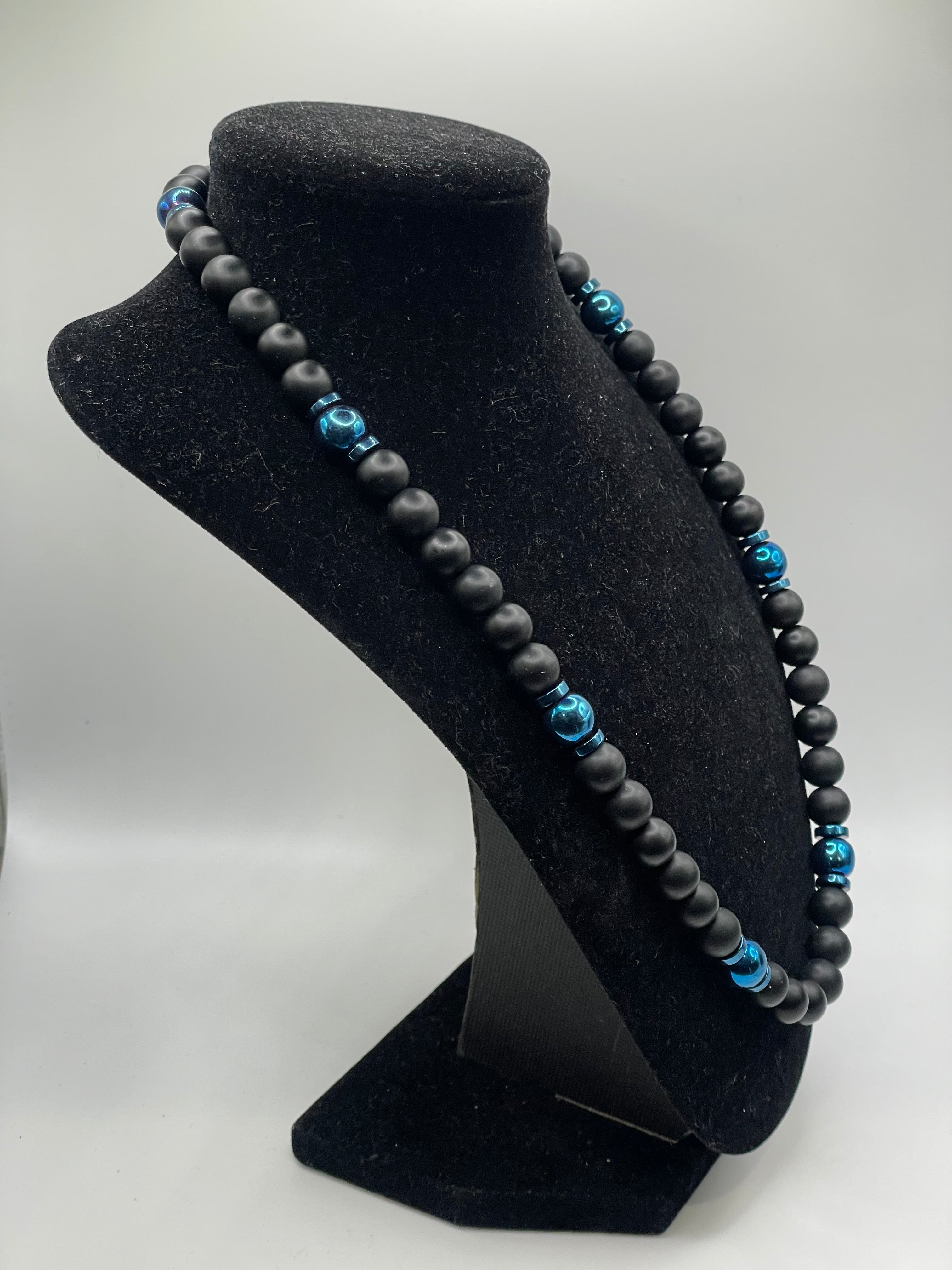 Black beaded necklace with blue beads on a black stand against a white background
