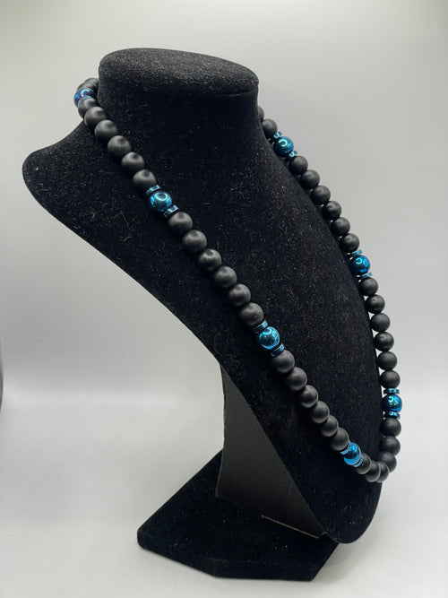 Black beaded necklace with blue beads on a black stand against a white background