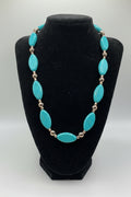 Turquoise necklace with gold accents on a black mannequin bust against a white background