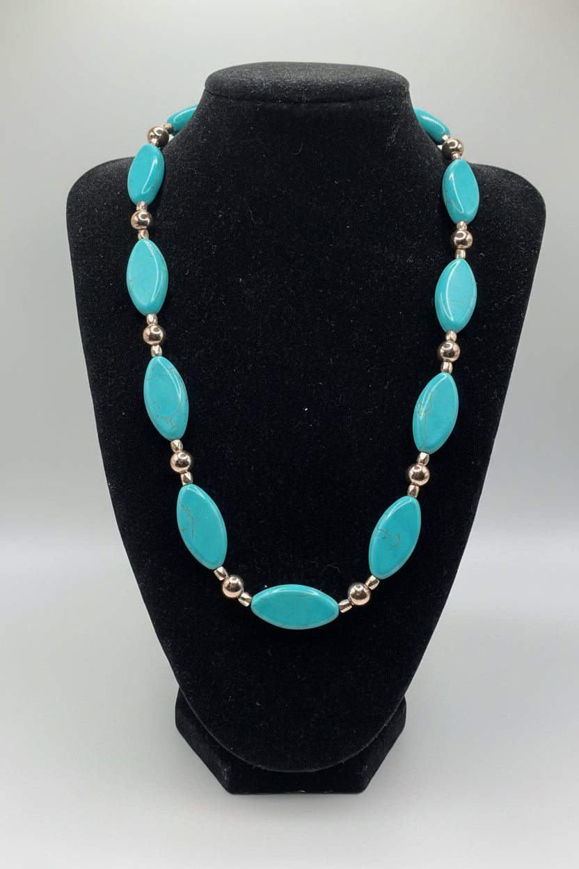 Turquoise necklace with gold accents on a black mannequin bust against a white background