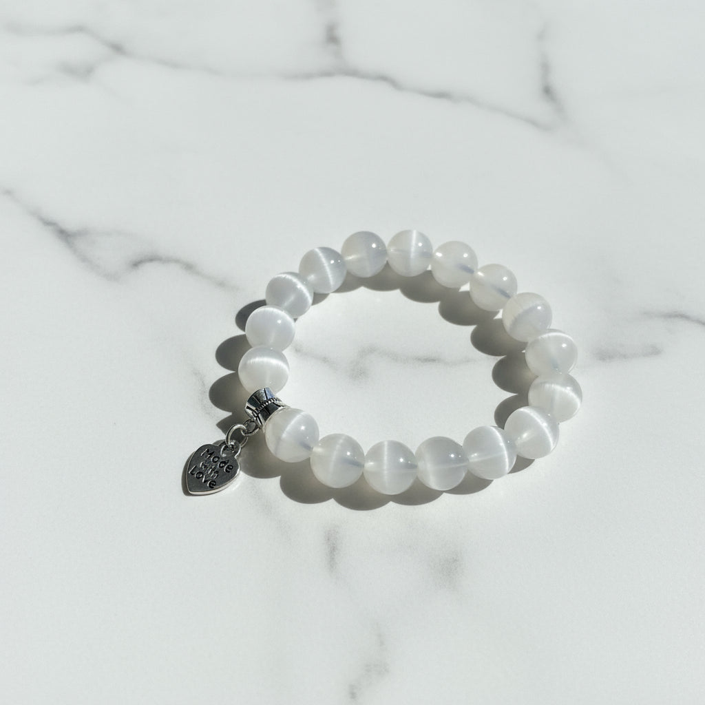 White beaded bracelet with a 'Made with Love' charm on a marble surface