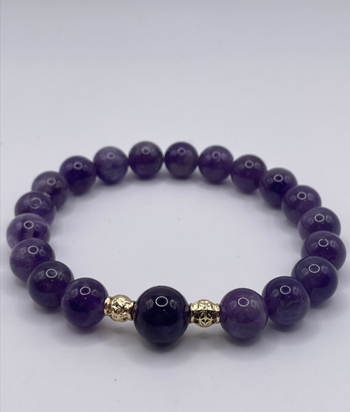 Purple beaded bracelet with gold accents on a white background
