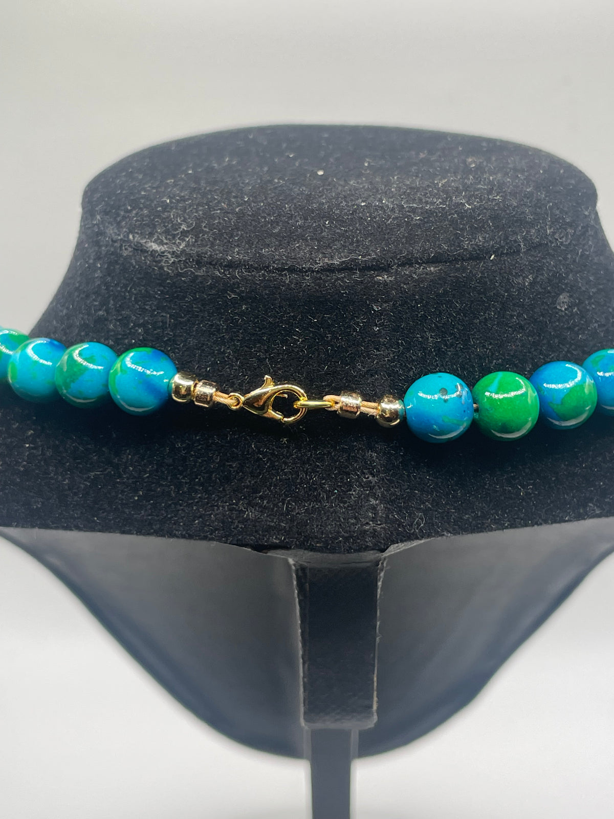 A beaded necklace with alternating turquoise blue and green marbled beads, displayed of The necklace features a gold-tone lobster clasp closure.